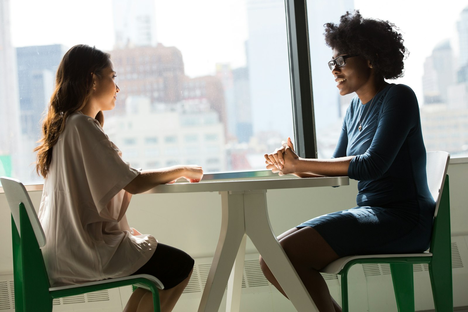 Two women talking across a table by a window